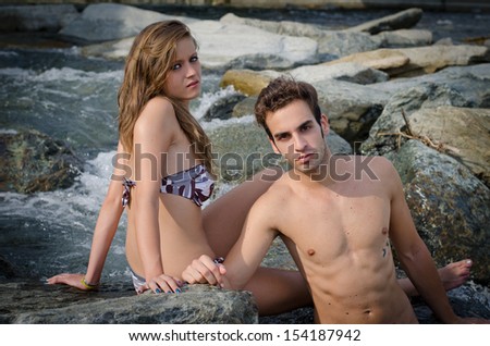 Romantic young couple in swimming suit on rocks by the sea or a river