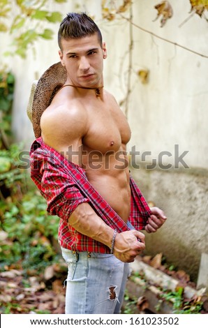Handsome, muscular young man with open shirt, jeans and straw hat outdoors