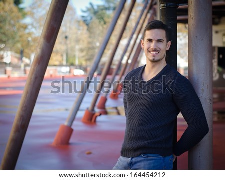 Smiling, friendly young man looking at camera, standing in urban structure
