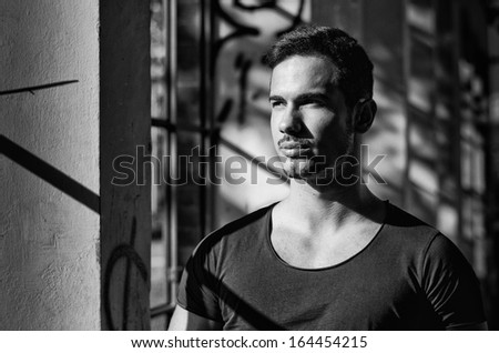 Black and white portrait of young man indoors next to windows looking out
