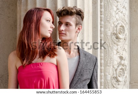 Elegant young couple standing in front of old stone column looking at each other