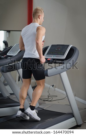 Blond attractive young man running on treadmill, seen from the back