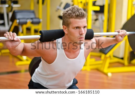 Handsome young man doing squats in gym with barbell