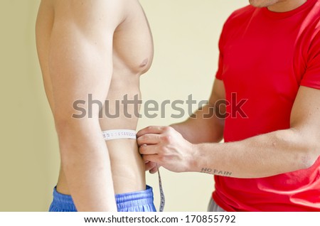 Personal trainer measuring shirtless muscular client\'s waist with tape meter
