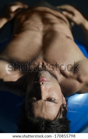 Muscular shirtless man laying down, belly up looking at camera