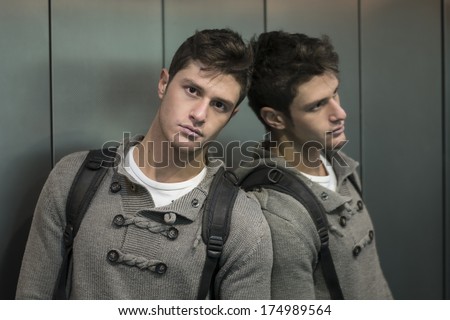 Handsome young man leaning against mirror inside an elevator (lift), looking at camera