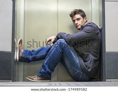 Handsome young man sitting in front of elevator (lift) doors, looking at camera