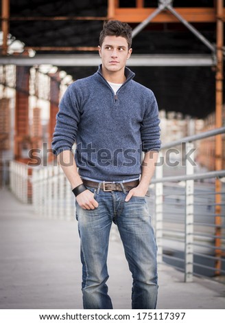 Handsome young man in industrial environment wearing sweater and blue jeans, looking to a side