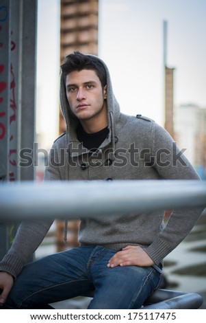 Handsome young man in industrial environment with wool hoodie and jeans, looking at camera