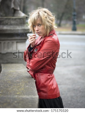 Pretty young woman smoking, wearing red leather jacket, outdoor photo