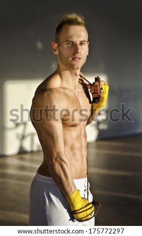 Shirtless muscular young man standing with jumping rope in gym, looking at camera
