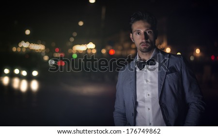 Attractive young man at night with city lights behind him, wearing elegant jacket and bowtie