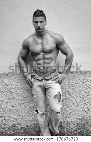 Attractive young man shirtless with jeans leaning against a wall, black and white shot