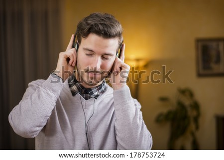 Attractive young man listening to music on headphones, eyes closed. Indoor shot in house