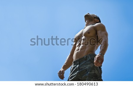 Muscular young male bodybuilder shirtless looking up in the sky, seen from below