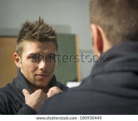 Handsome young man looking at himself in mirror with a grin