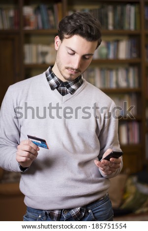 Attractive young man shopping online with mobile phone, holding credit card