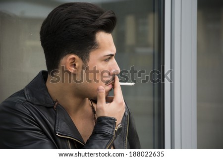 Handsome young man with leather jacket smoking a cigarette, looking away