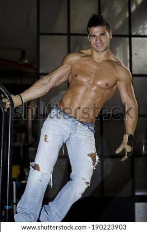 Muscular latino bodybuilder in jeans hanging from metal handle, showing ripped body