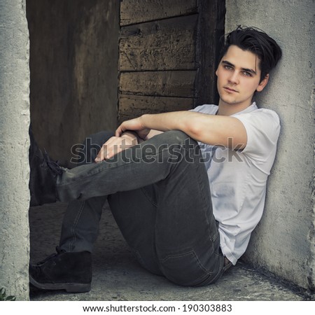 Attractive young man sitting on old door's threshold looking at camera