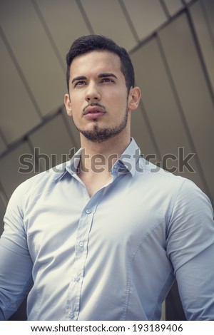 Handsome young man outside wearing shirt, looking away. Shot from below