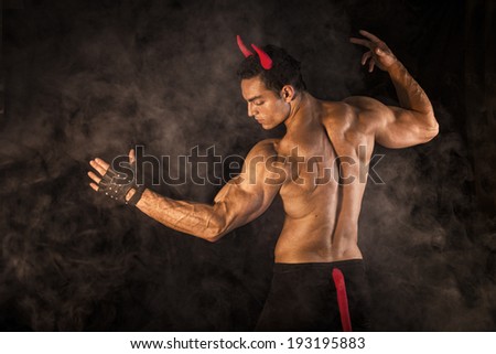 Shirtless muscular male bodybuilder dressed with devil costume on dark background