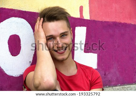 Attractive young blond man against colorful graffiti wall smiling with tongue out of his teeth