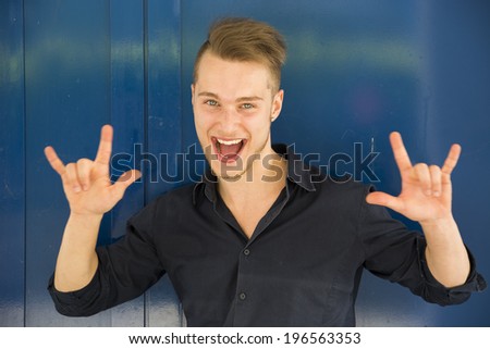 Happy handsome young man screaming and doing I Love You hand sign