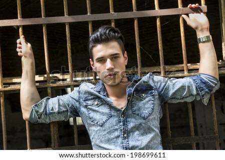 Handsome black haired young man in denim shirt against metal cage bars