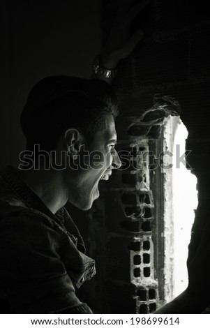 Young man indoor screaming out through hole in the wall, black and white shot