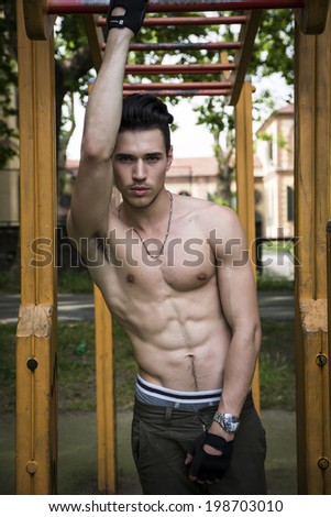 Attractive shirtless young man exercising and working out in outdoor gym in city park