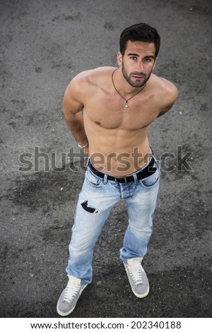 Handsome bearded shirtless young man standing on asphalt ground, looking at camera, shot from above