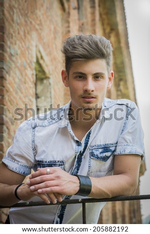 Handsome young man outdoors leaning on hand-rail, looking down at camera