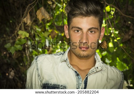 Handsome young man looking at camera. Plants and bushes around him