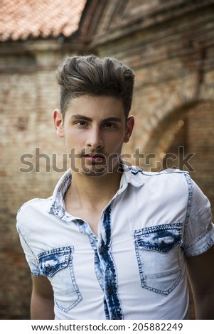 Handsome young man outdoors in front of old house or palace, looking at camera
