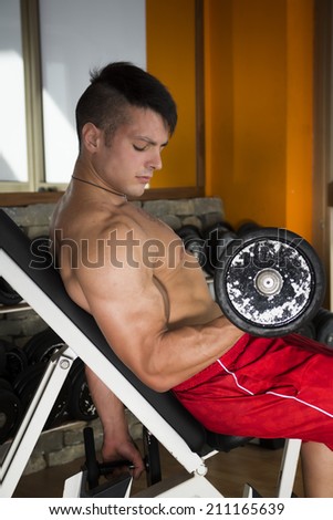 Fit muscular shirtless young man working out with weights in a gym to strengthen and tone his muscles in a health, exercise and fitness concept
