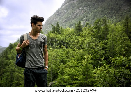 Handsome muscular young man backpacking or hiking in lush green mountain scenery pausing to look at something  on the ground
