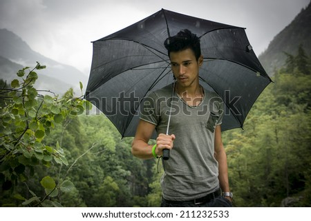 Smiling handsome young man holding an umbrella on a stormy day as he takes a walk along a trail in the mountains