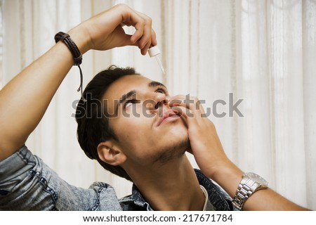 Handsome young man dropping medicine in his eye with eye-dropper