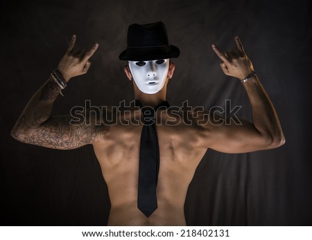 Shirtless man dancer or actor with creepy, scary mask at back of his head on dark background