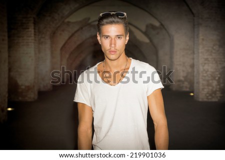 Handsome young man in old building walking inside gallery, looking at camera