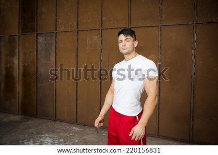Attractive young muscular man portrait in white shirt and red gym suit pants posing