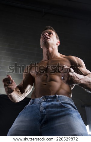 Low angle close up view of a strong young man with a muscular physique standing clenching his fists to emphasize his arm and shoulders muscles