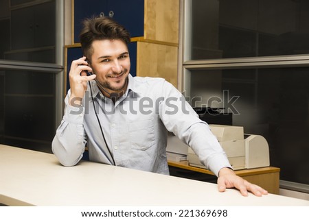 Businessman or customer (support) service man taking a call on his headset phone as he sits at a table in the office looking up to smile at the camera as he listens to the conversation