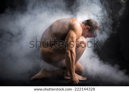 Nude Profile of Young Muscle Man Crouching in Fog in Studio with Black Background
