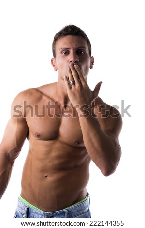 Sexy handsome shirtless man with a muscular physique standing blowing a kiss with his hand to his mouth or hiding a guilty expression, isolated on white