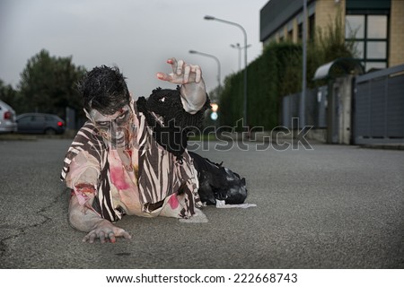Male zombie crawling on his knees, on empty city street, looking at camera reaching out one hand. Halloween theme