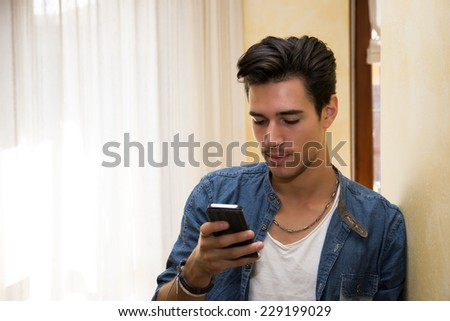 Attractive young man typing on cell phone, indoor shot in house living room