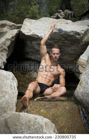 Handsome young muscle man sitting in water pond, naked wearing only swimming suit