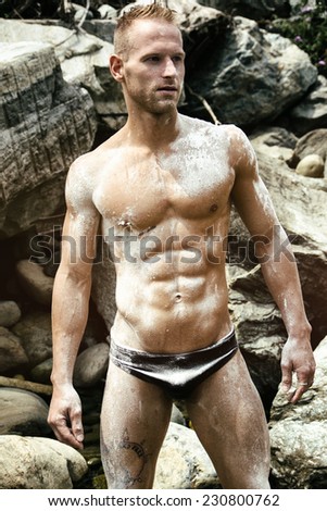 Handsome young muscle man standing naked wearing only swimming suit, with white powder all over body